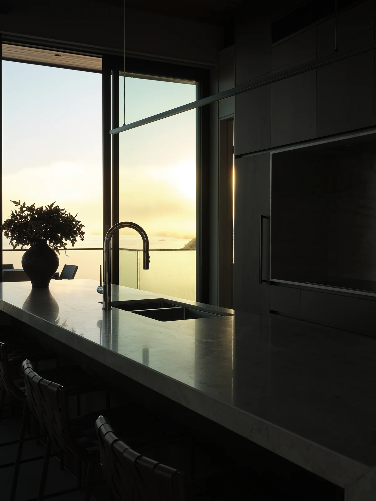 Sunrise beyond the kitchen sink and stone bar with the walnut cooking wall alongside