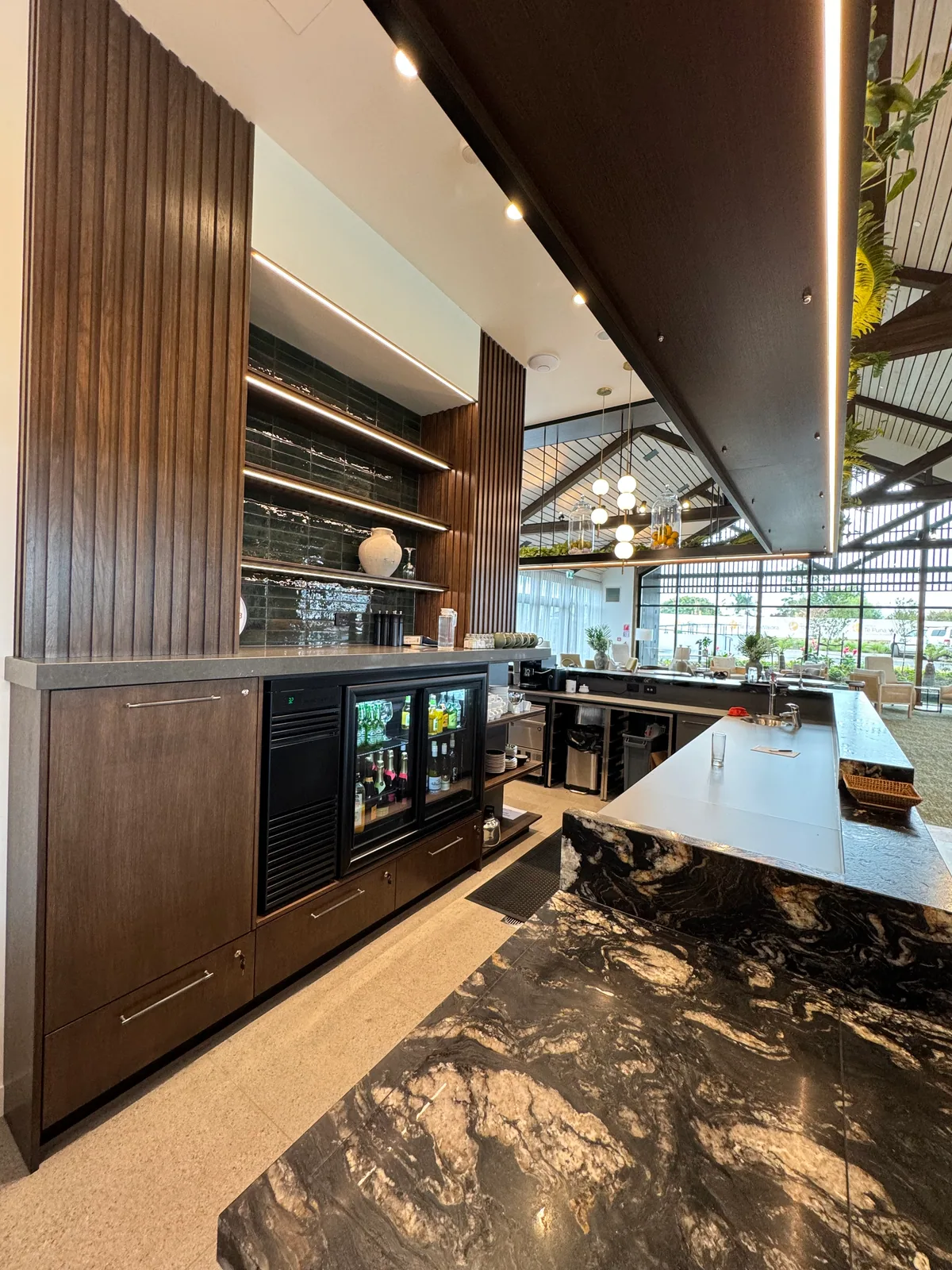 Inside the Arvida bar showing timber cabinetry, illuminated shelving, refrigeration and stone worktops