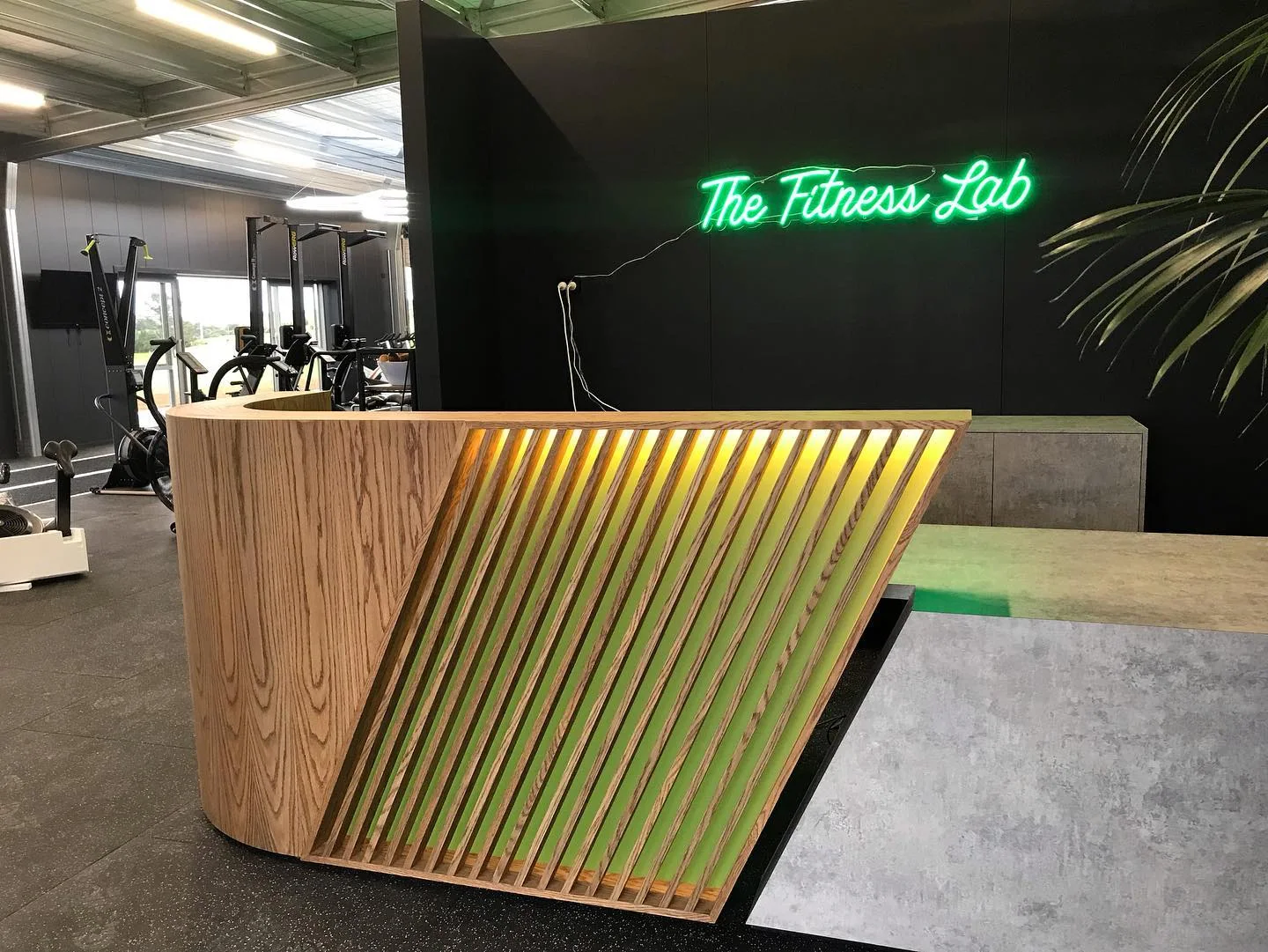 Custom timber reception counter with angled slats, integrated green lighting and concrete-look surfaces