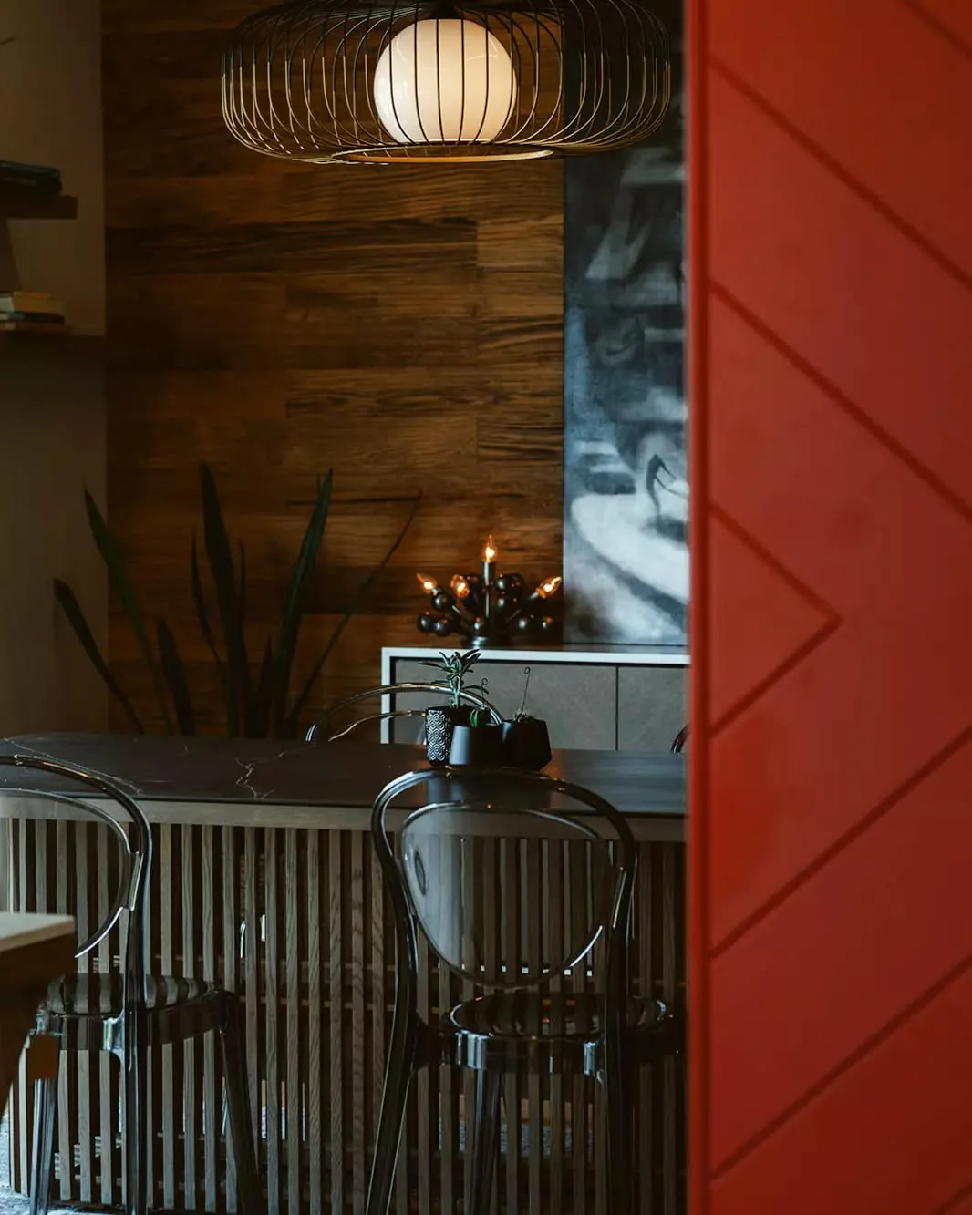 View through a red feature door to custom timber screening, dining joinery and decorative lighting