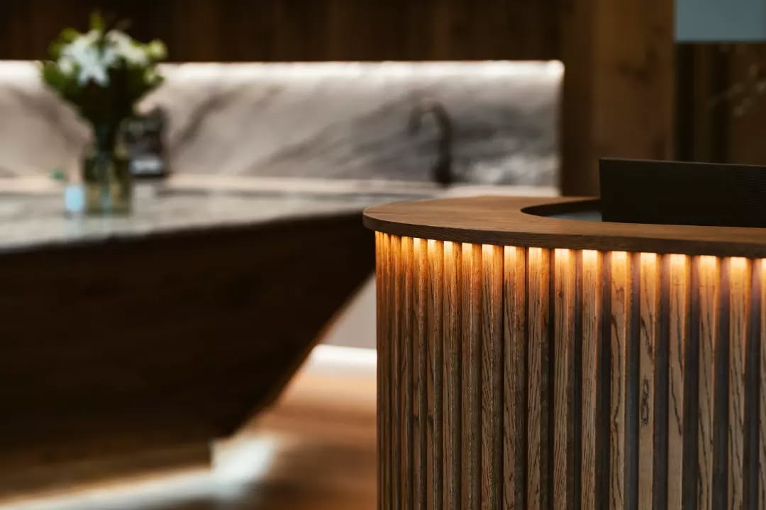 Close detail of a rounded timber-slat counter with concealed warm lighting