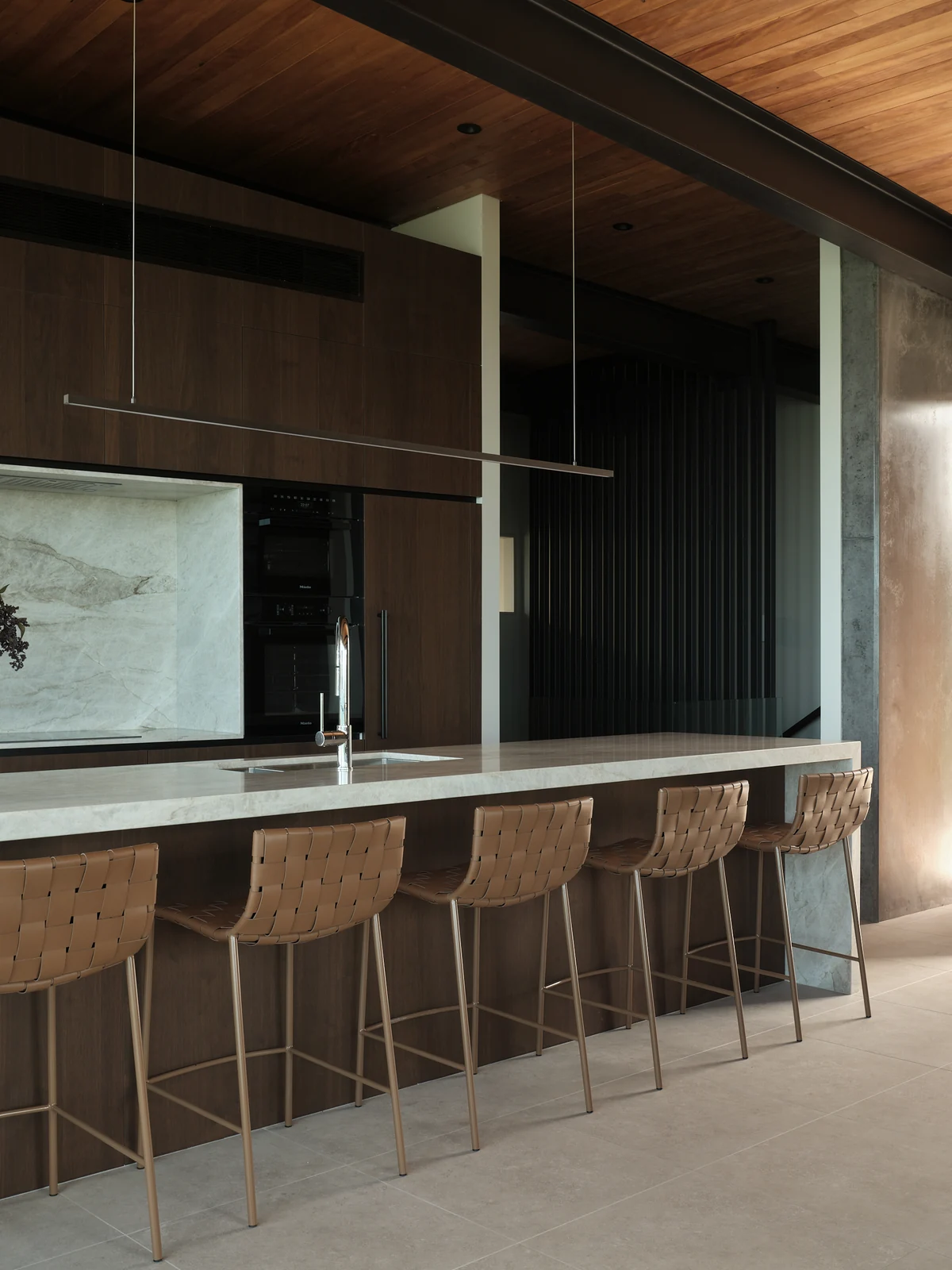 Honed stone breakfast bar with woven stools beneath full-height walnut cabinetry
