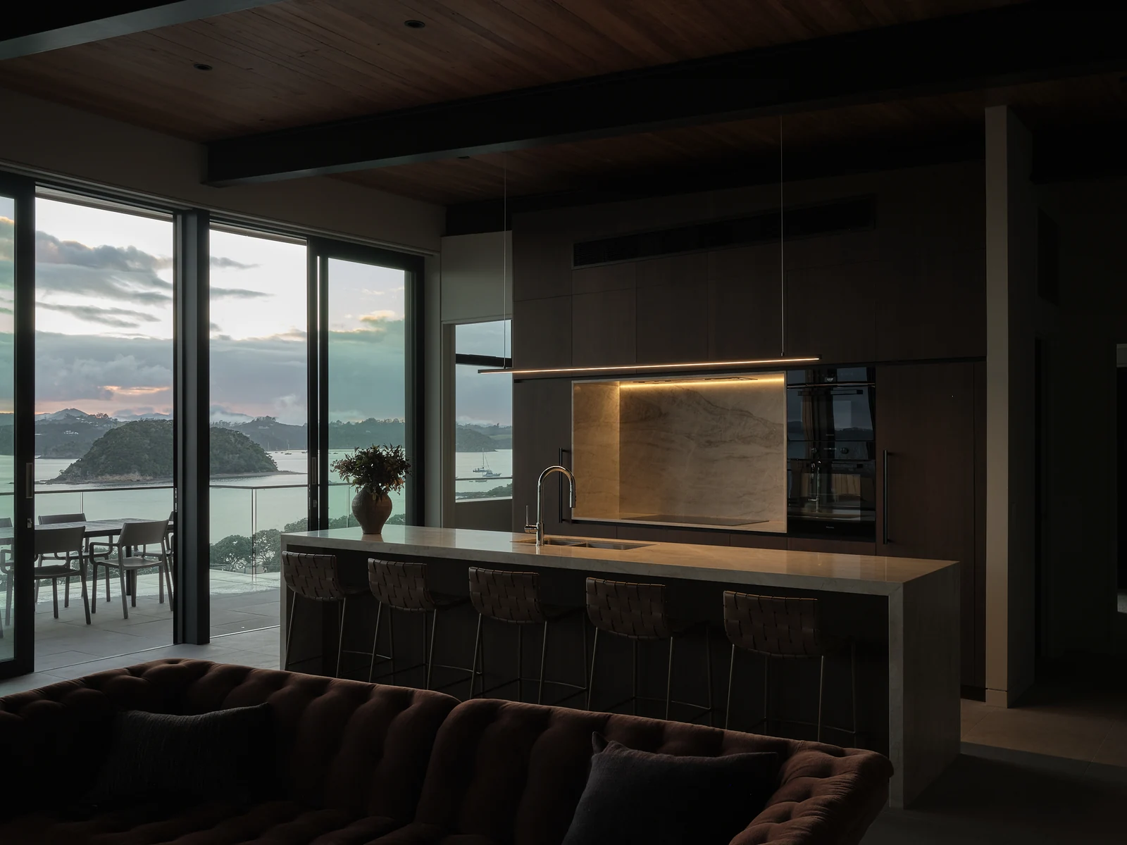 The same side of the kitchen at dawn with illuminated stone splashback and island pendant