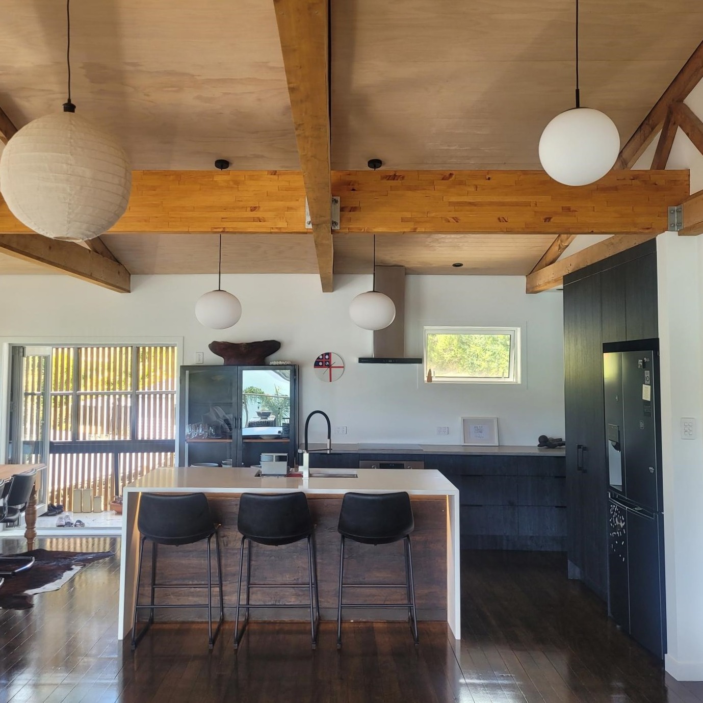 Dark kitchen and island beneath exposed timber beams and pendant lighting