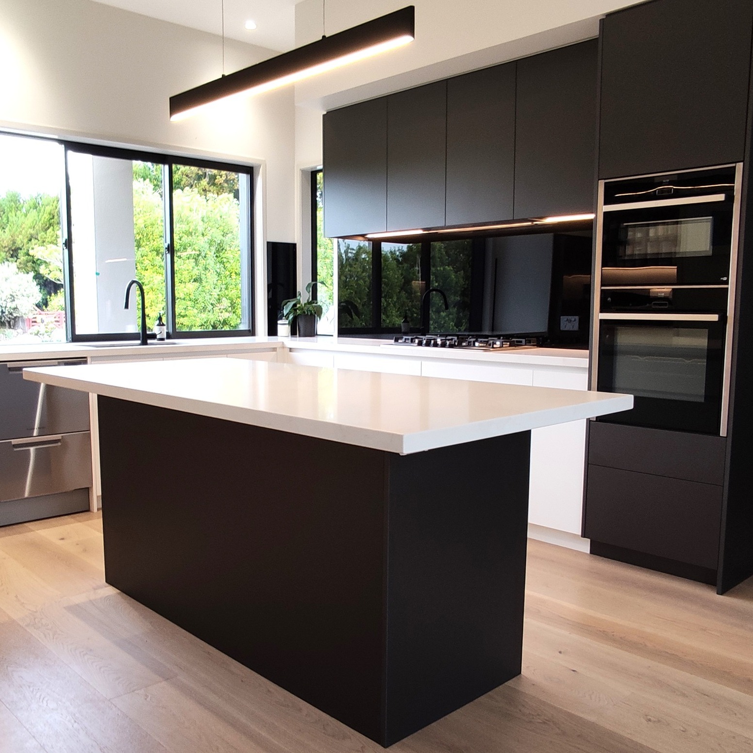 Black kitchen and island with white worktops, full-height cabinetry and a garden outlook