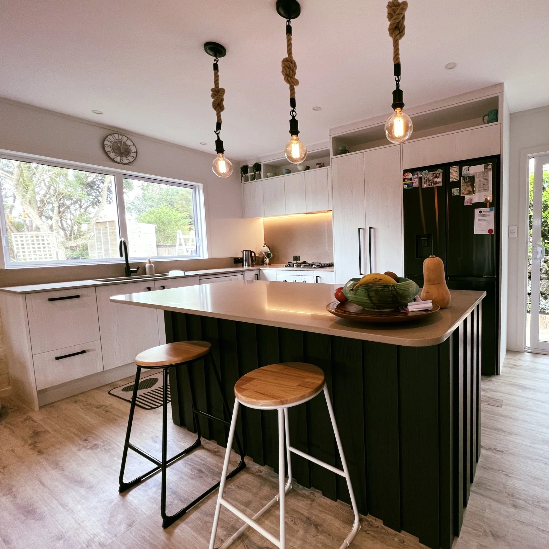 White Shaker kitchen with a black island, timber stools and rope pendant lights
