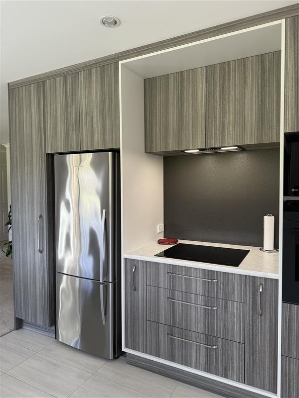 Compact grey timber-look kitchen cabinetry with integrated refrigerator and cooktop
