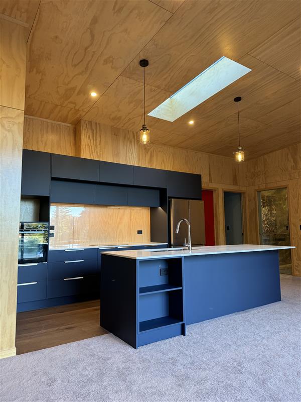 Navy kitchen cabinetry and island set within a warm plywood interior by North Interiors