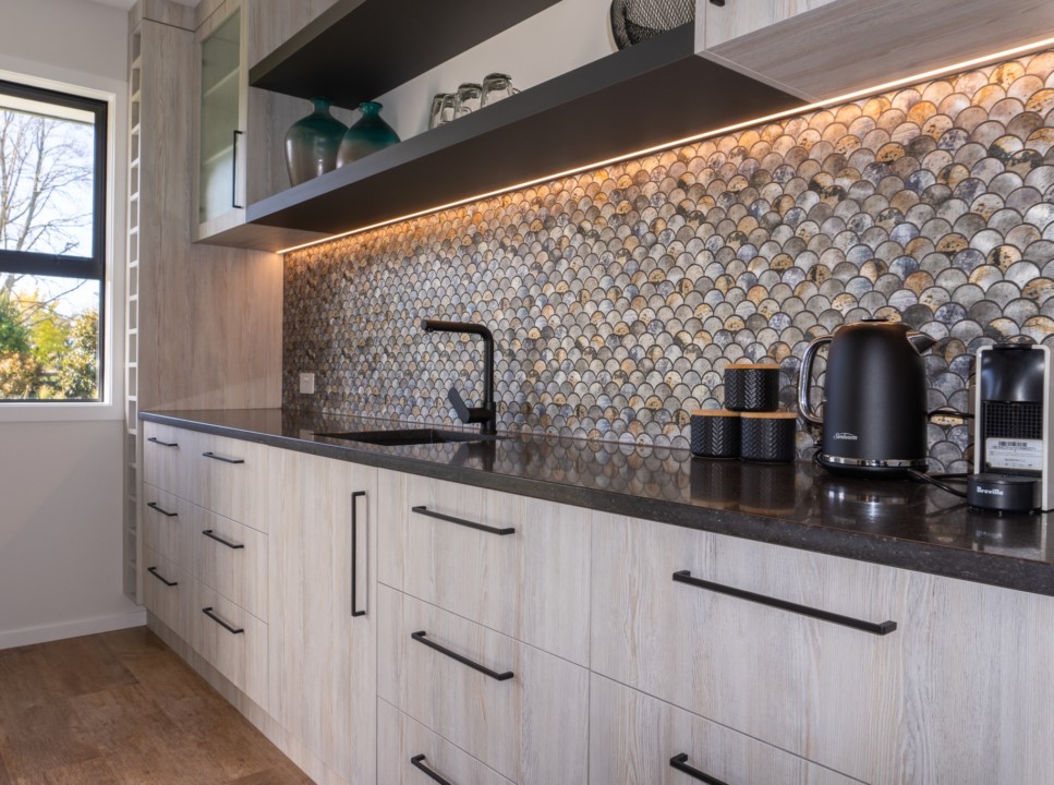Timber-look kitchen drawers with dark benchtop, open shelving and shell-pattern splashback