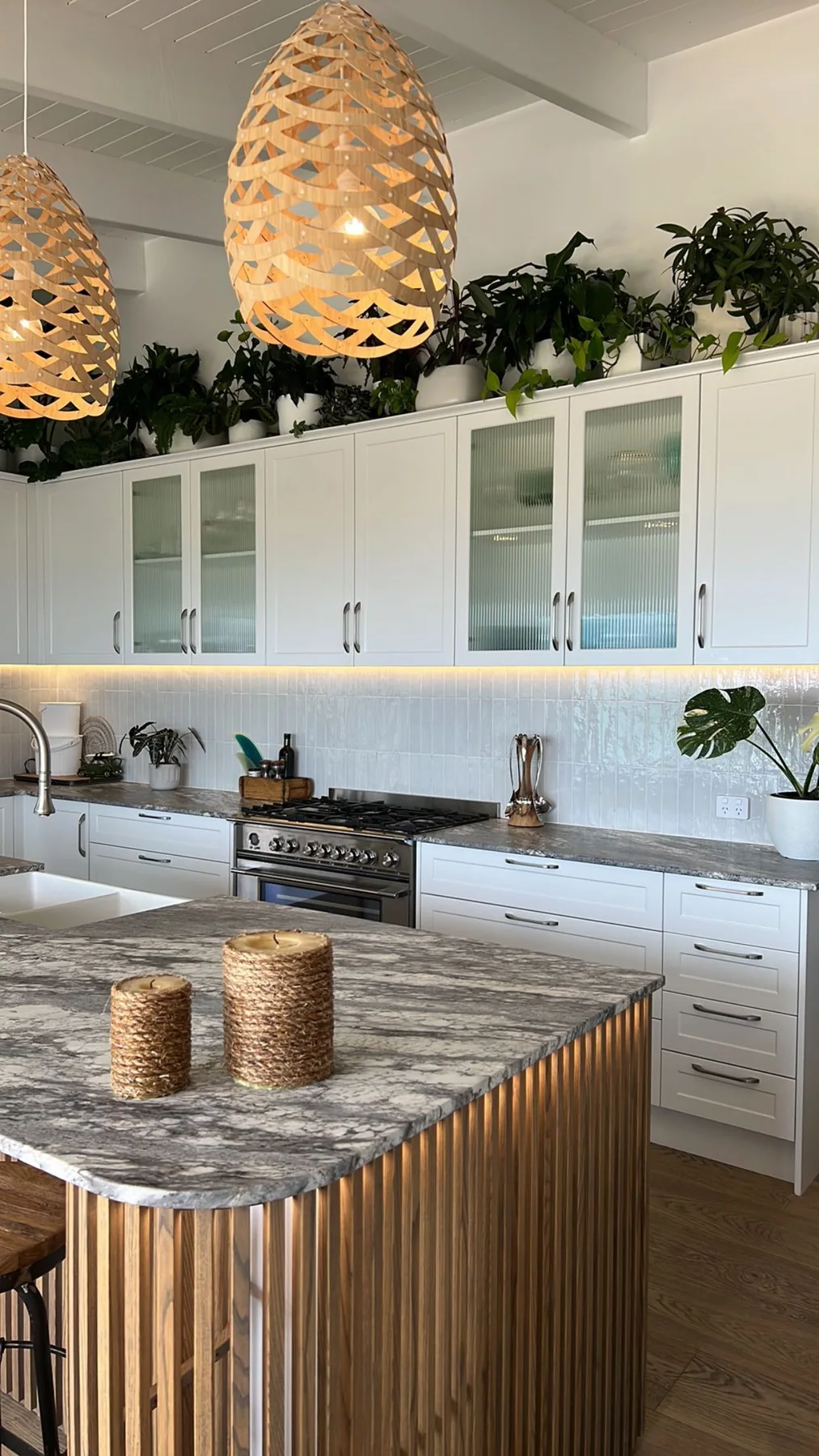 Close portrait view of the curved timber-slat kitchen island, stone worktop and woven pendants