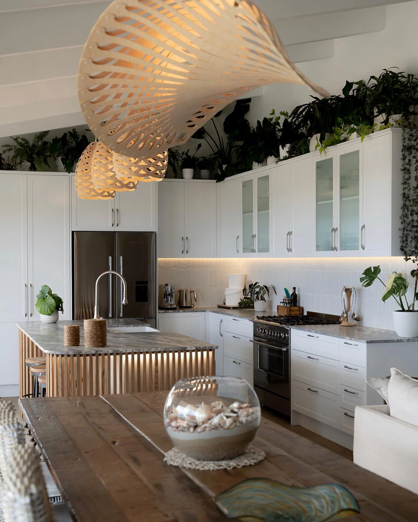 White kitchen and curved timber-slat island viewed from the adjoining dining area