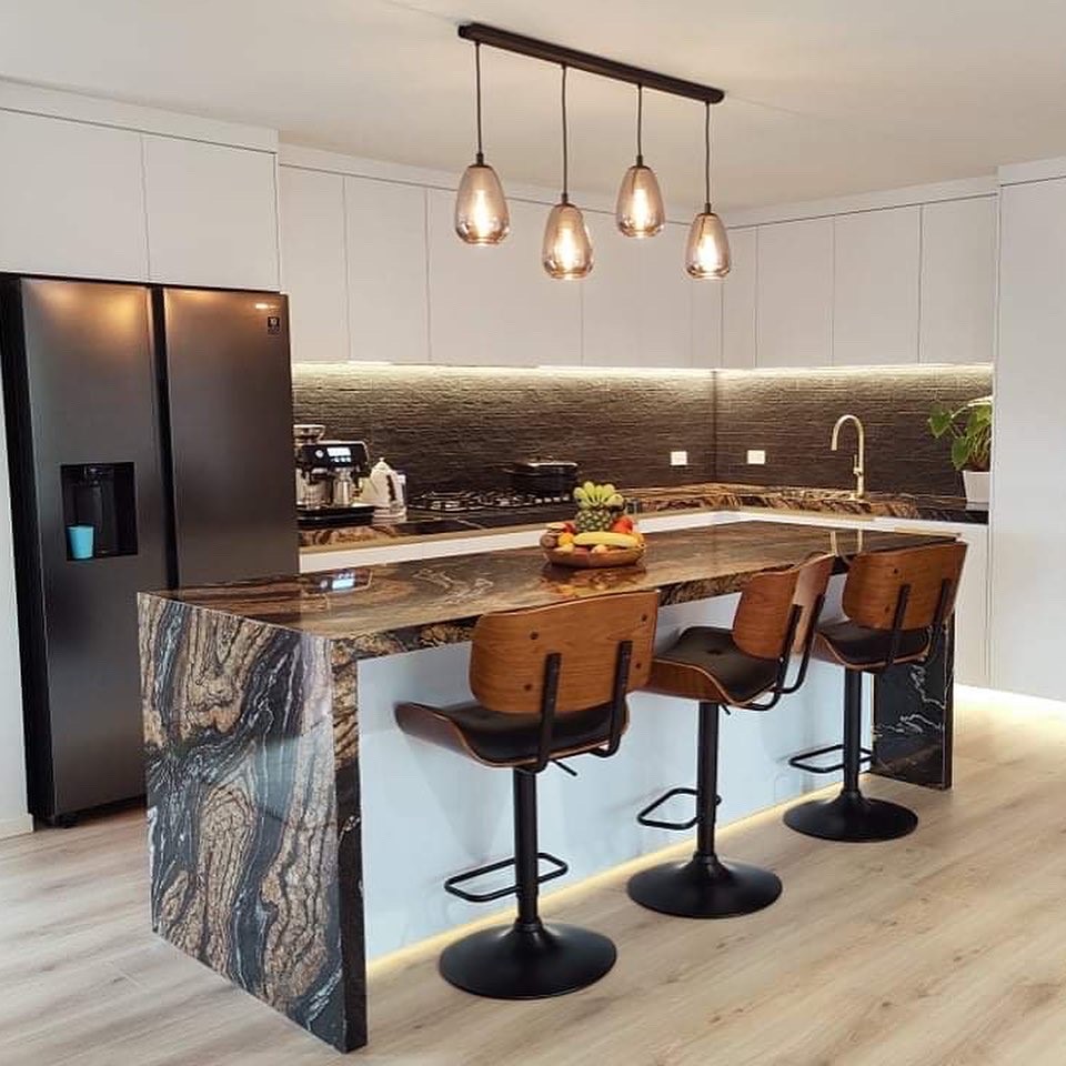 White kitchen with a dramatic stone waterfall island and timber bar stools