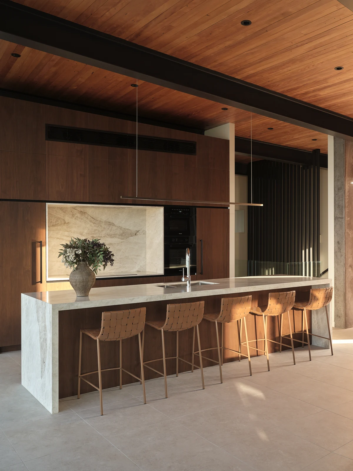 Late afternoon sun across the walnut cabinetry, stone island and woven kitchen stools