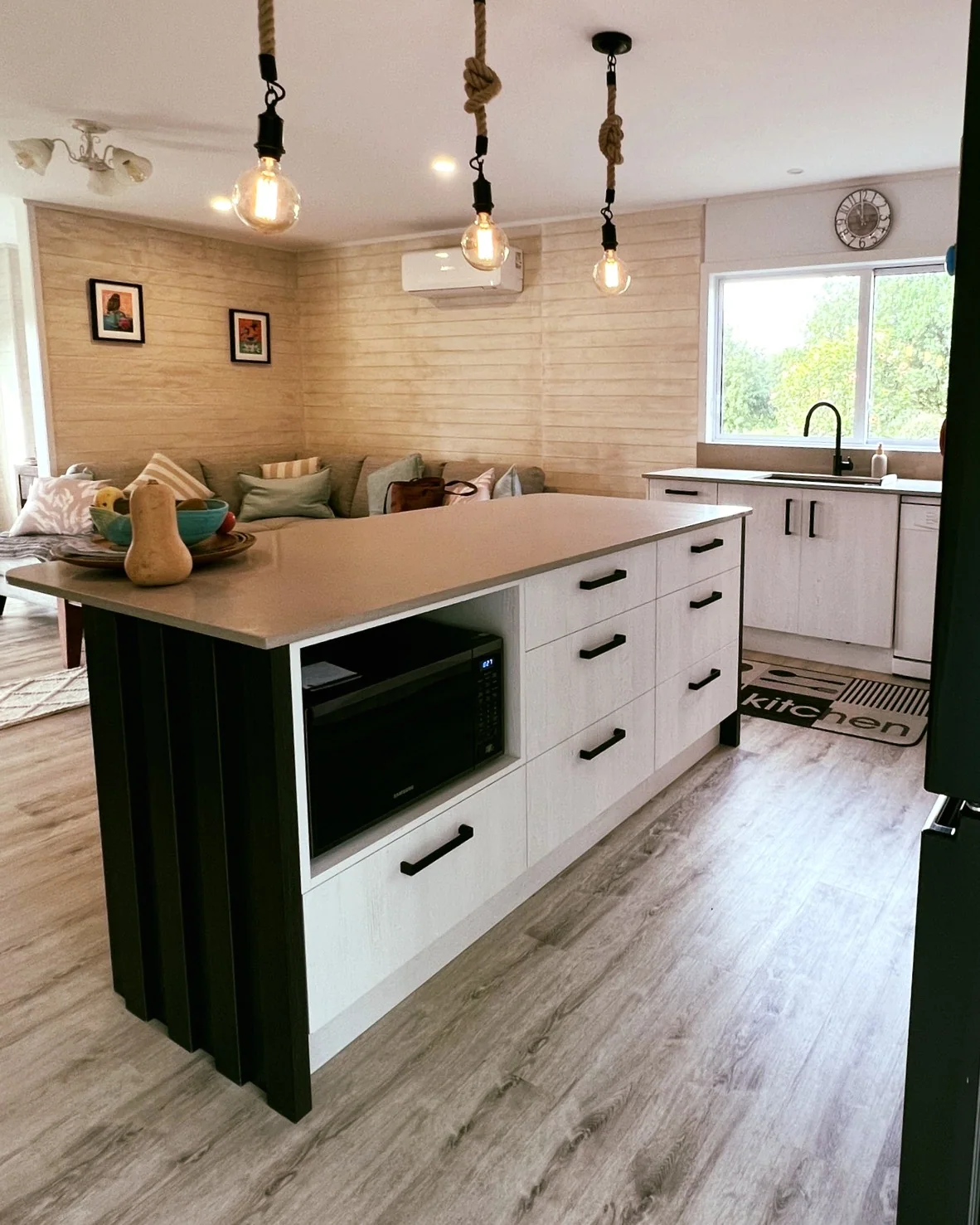 White kitchen with black island end panels, integrated appliances and exposed-bulb pendant lights