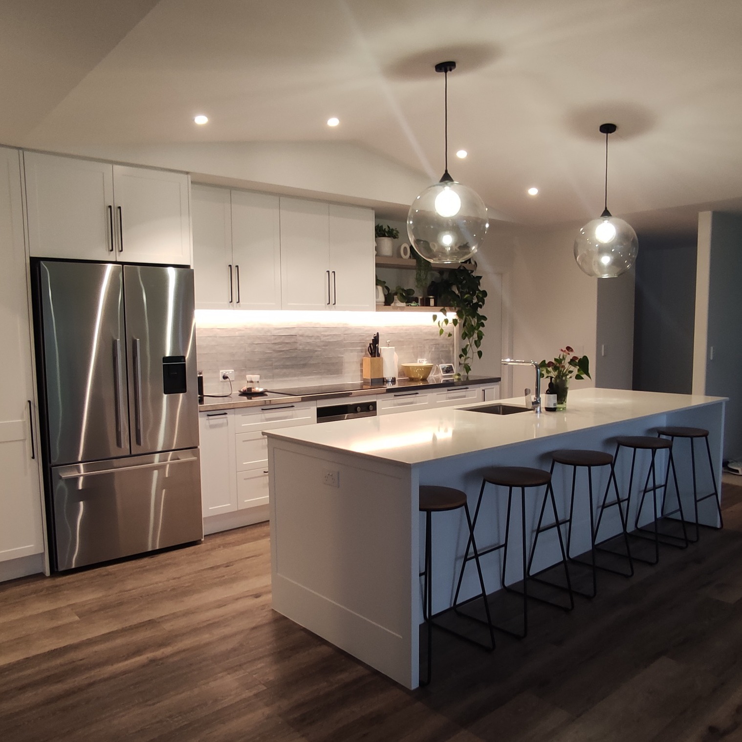 White kitchen with illuminated island, glass pendants and dark bar stools
