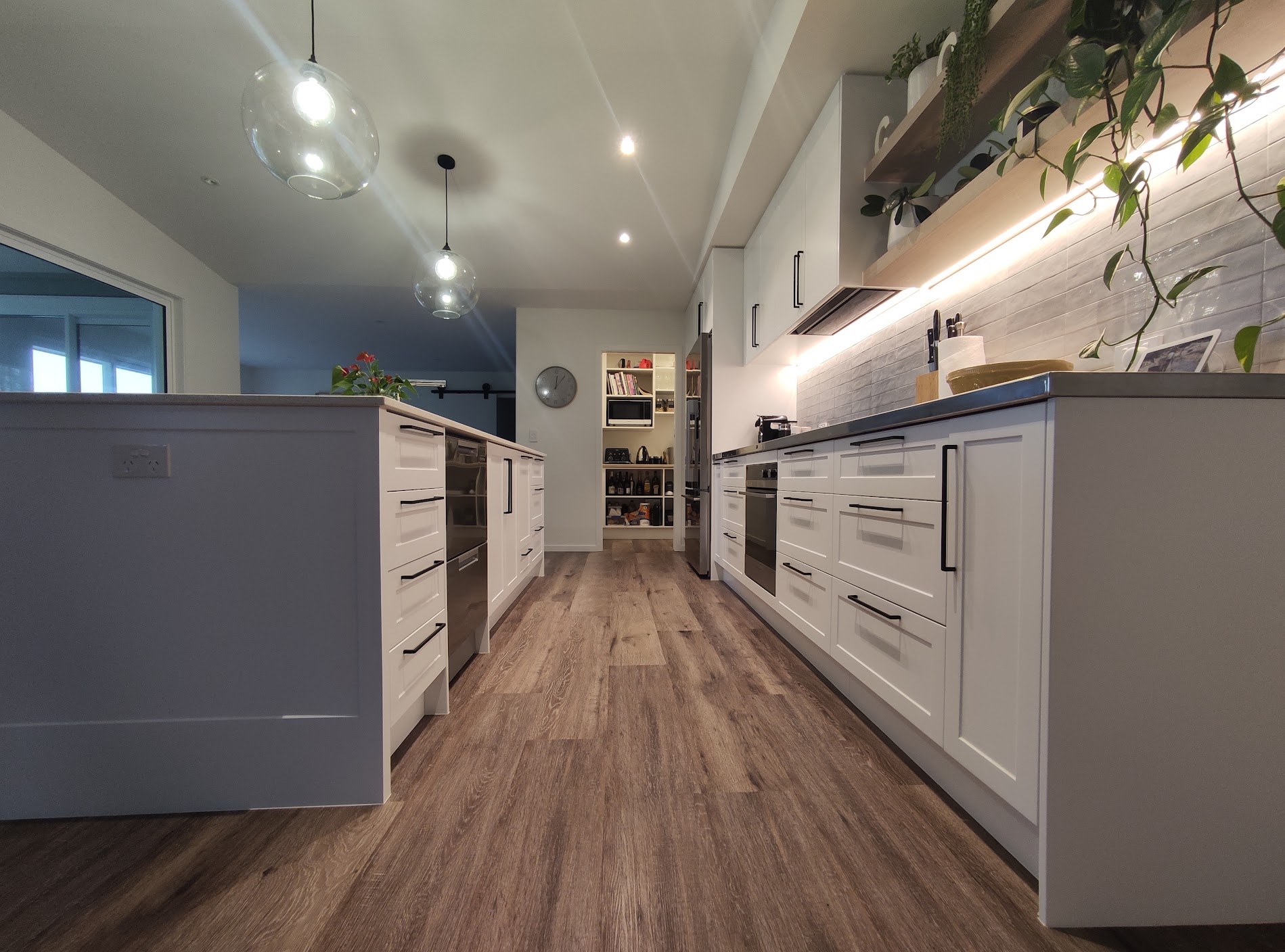 Long white Shaker kitchen with black handles, timber floors and open pantry storage