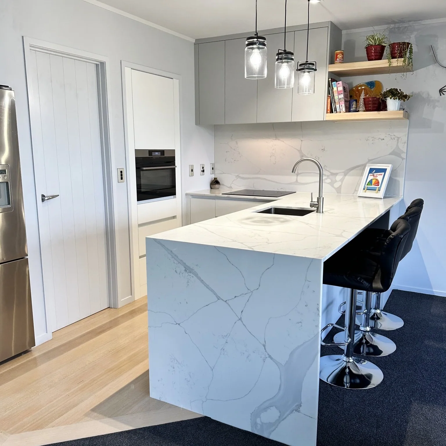Compact white kitchen with a stone waterfall peninsula, integrated seating and glass pendant lights