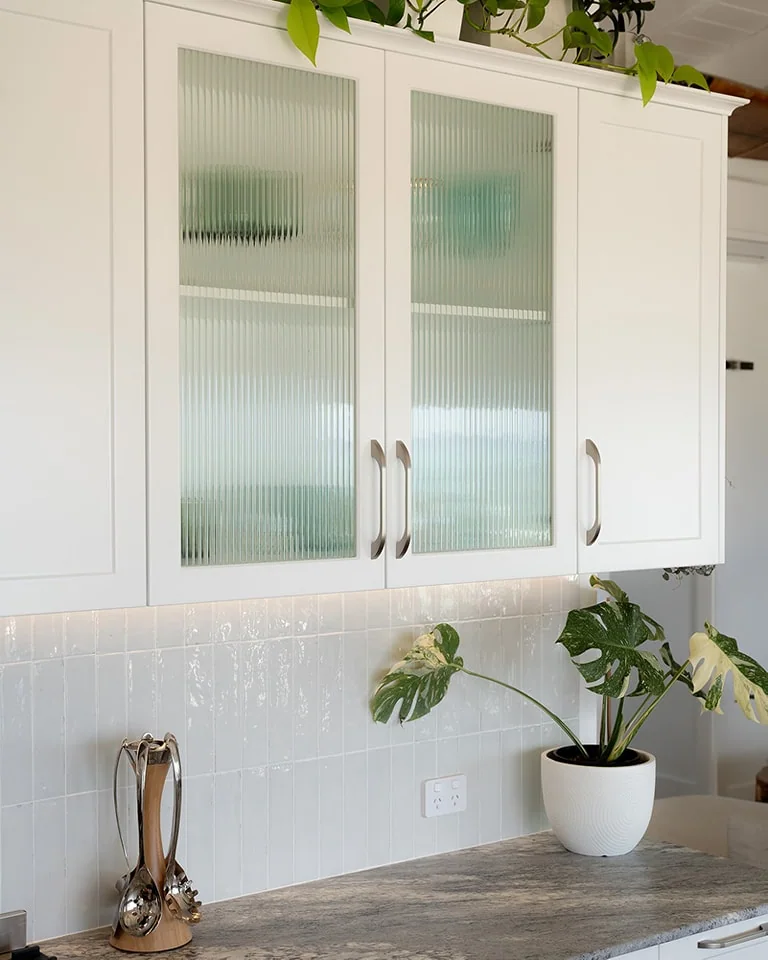 White utility cabinetry with fluted glass doors, stone worktop and softly lit tiled splashback