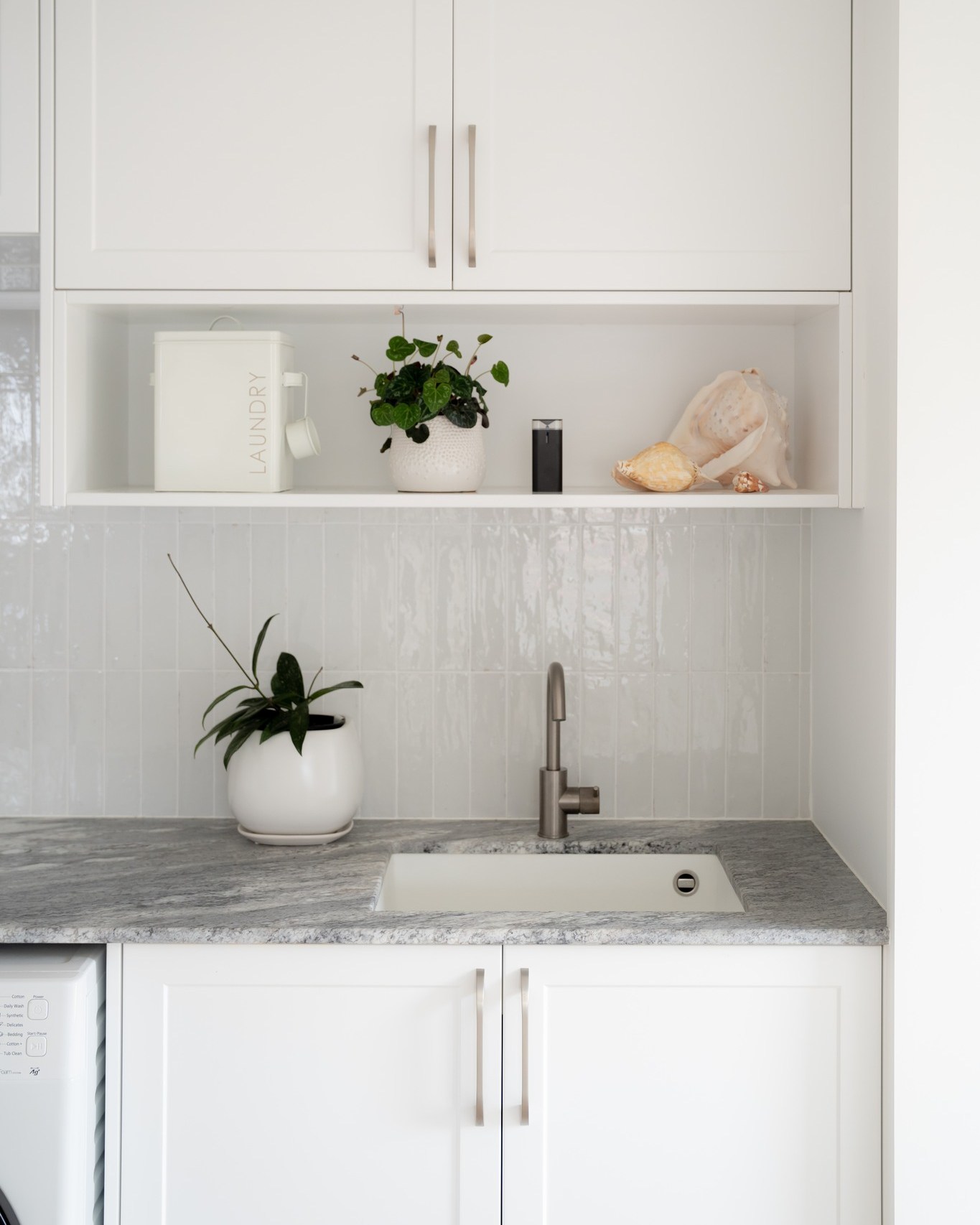 Bright white laundry cabinetry with stone benchtop, integrated sink, open shelf and overhead storage by North Interiors