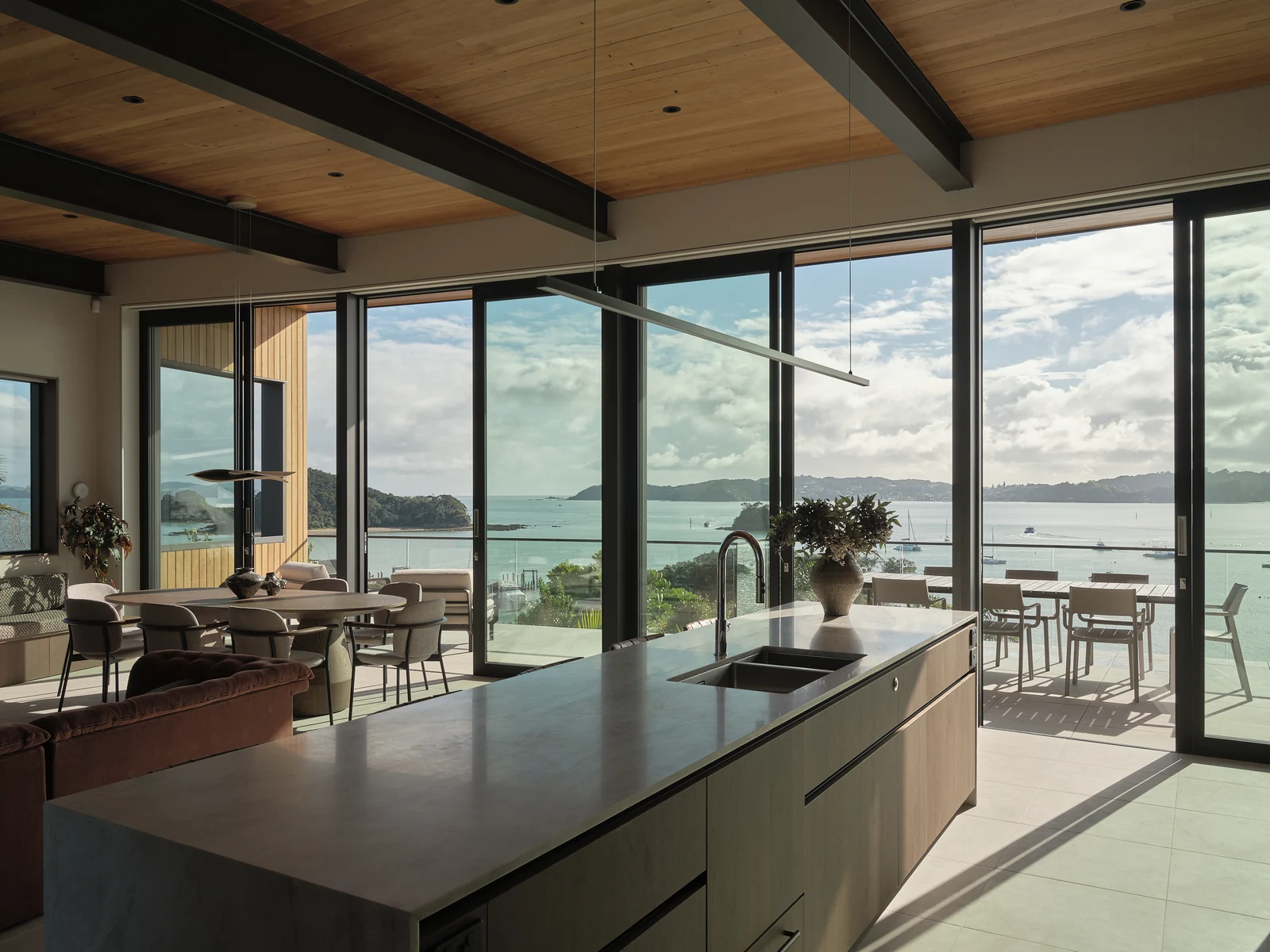 View across the long kitchen island towards the dining table, open terrace and bay