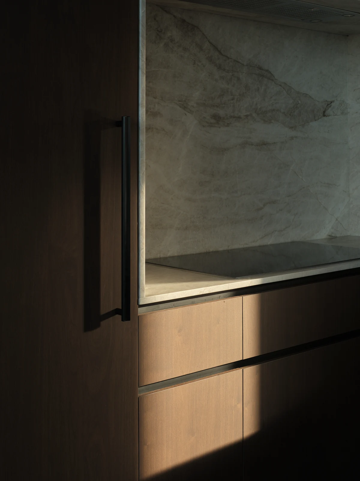 Sunlight on the stone-lined cooking recess beside tall walnut cabinetry