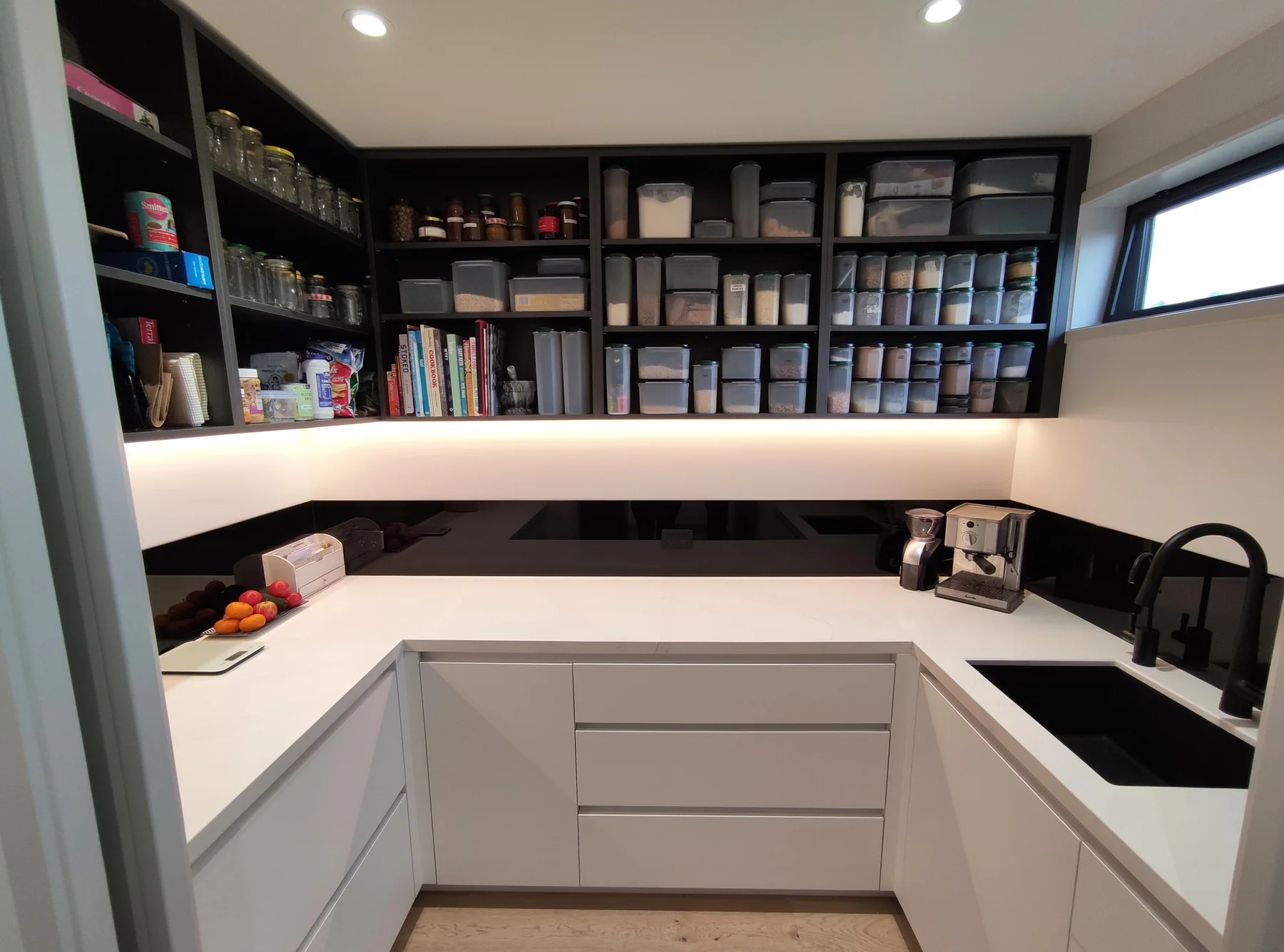 Custom scullery with full-height open pantry storage, white worktops and integrated task lighting by North Interiors