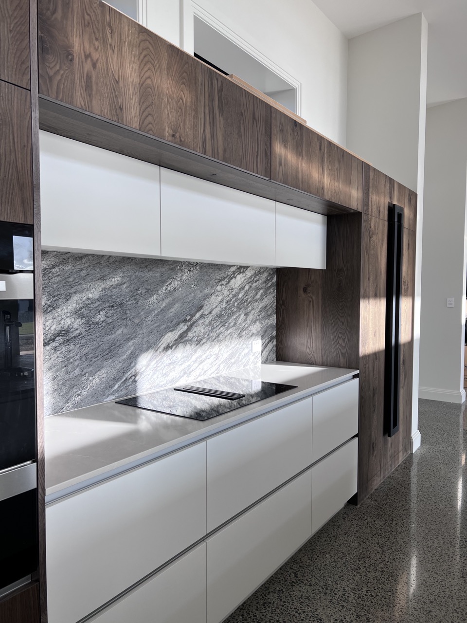 Walnut and white scullery cabinetry with a stone splashback and integrated cooktop by North Interiors