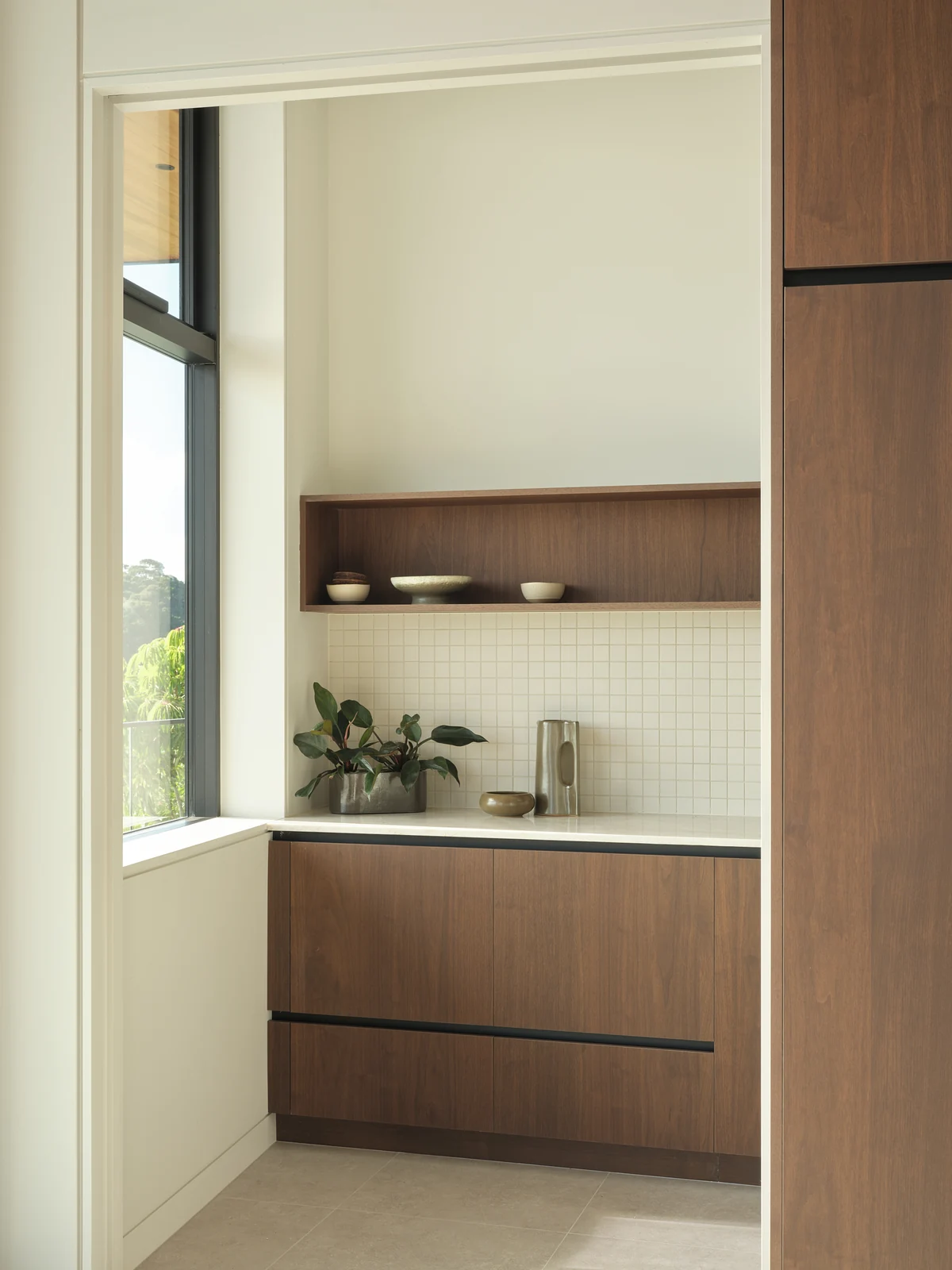 Walnut scullery cabinetry and pale stone worktop beside a tall window