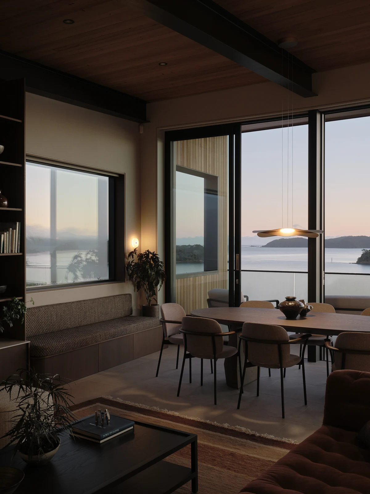 The full window seat beside the dining table at dawn with the pendant and wall light illuminated