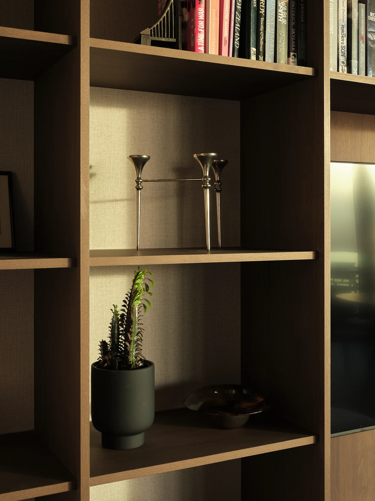 Sunlight picks out books, objects and the slender edges of the living room shelves