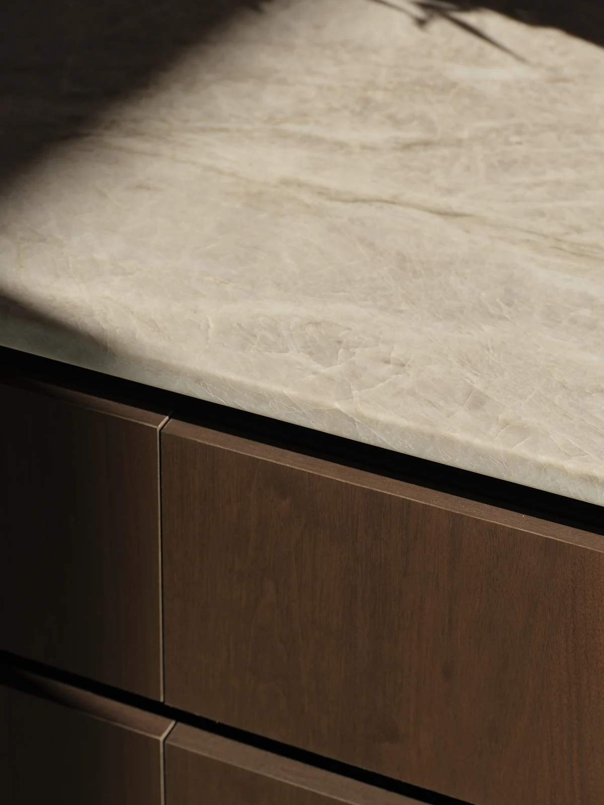 Honed stone worktop meeting a fine dark reveal above warm walnut drawer fronts