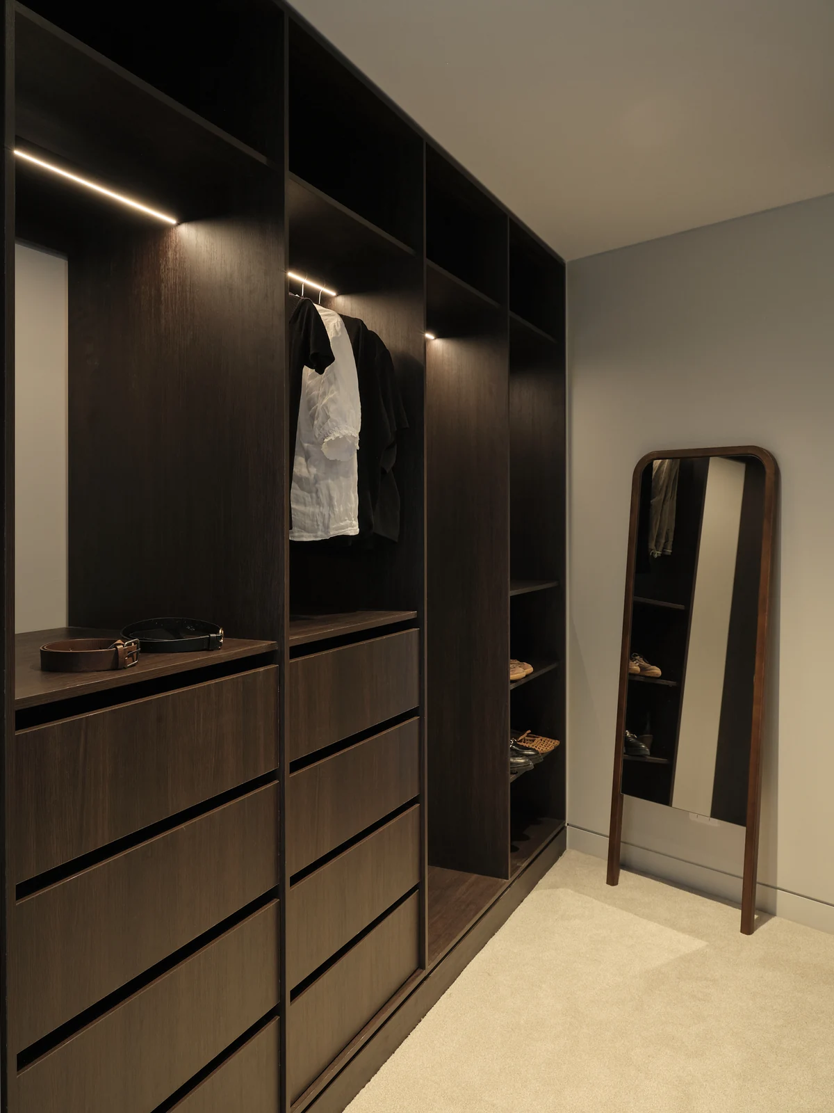 Dark timber master wardrobe with open hanging bays, drawer banks and integrated lighting