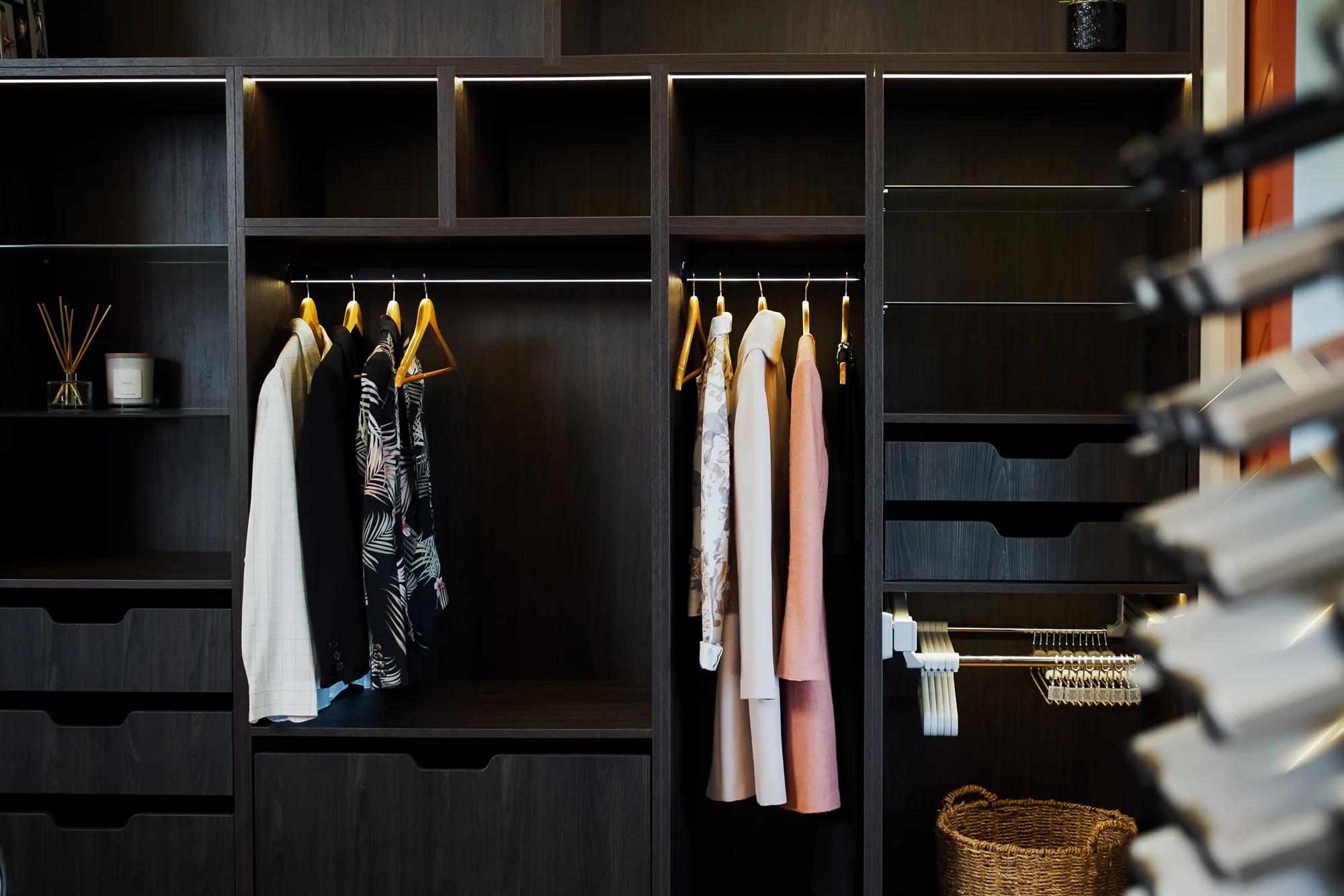 Dark timber wardrobe with illuminated hanging bays, open shelving and fitted drawers by North Interiors